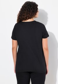 Zwarte t-shirt met korte mouwen en een ronde hals. Zachte stof, ontspannen pasvorm en rechte zoom. Achteraanzicht dat textuur en kleur laat zien.