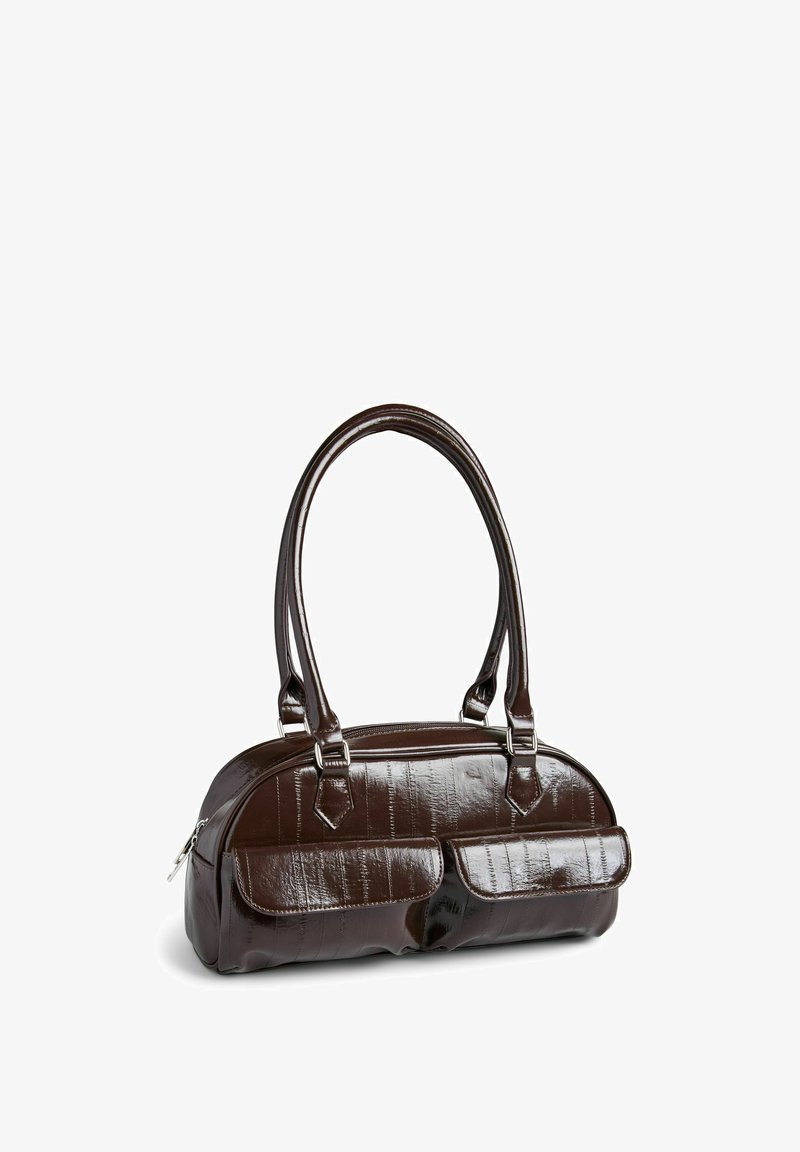 Petit sac à main en cuir verni marron foncé avec deux poches avant à rabat et double bandoulière, posé sur une surface blanche.
