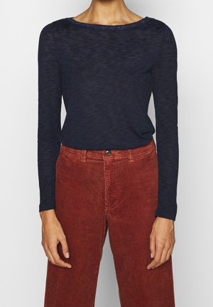 Maglietta a maniche lunghe blu navy con scollatura ampia e una sottile trama, abbinata a pantaloni in corduroy ruggine a vita alta con strisce verticali.
