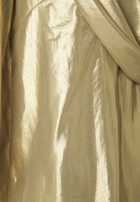 Tessuto dorato lucido e metallico con una texture liscia. Presenta morbidi drappeggi e una leggera lucentezza, evidenziando pieghe e creste.