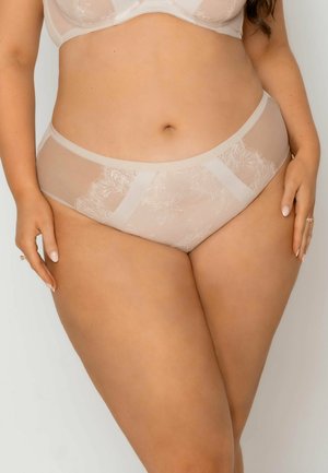 Kobieta w cielistym koronkowym komplecie bielizny, ukazująca środkową część ciała i górną część ud na jednolitym jasnym tle.