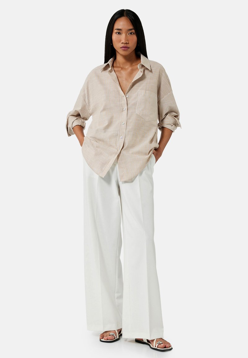 Beige en witte gestreepte button-up shirt met opgerolde mouwen, gecombineerd met wijde witte broeken en zwarte sandalen. Soepele, ontspannen pasvorm.