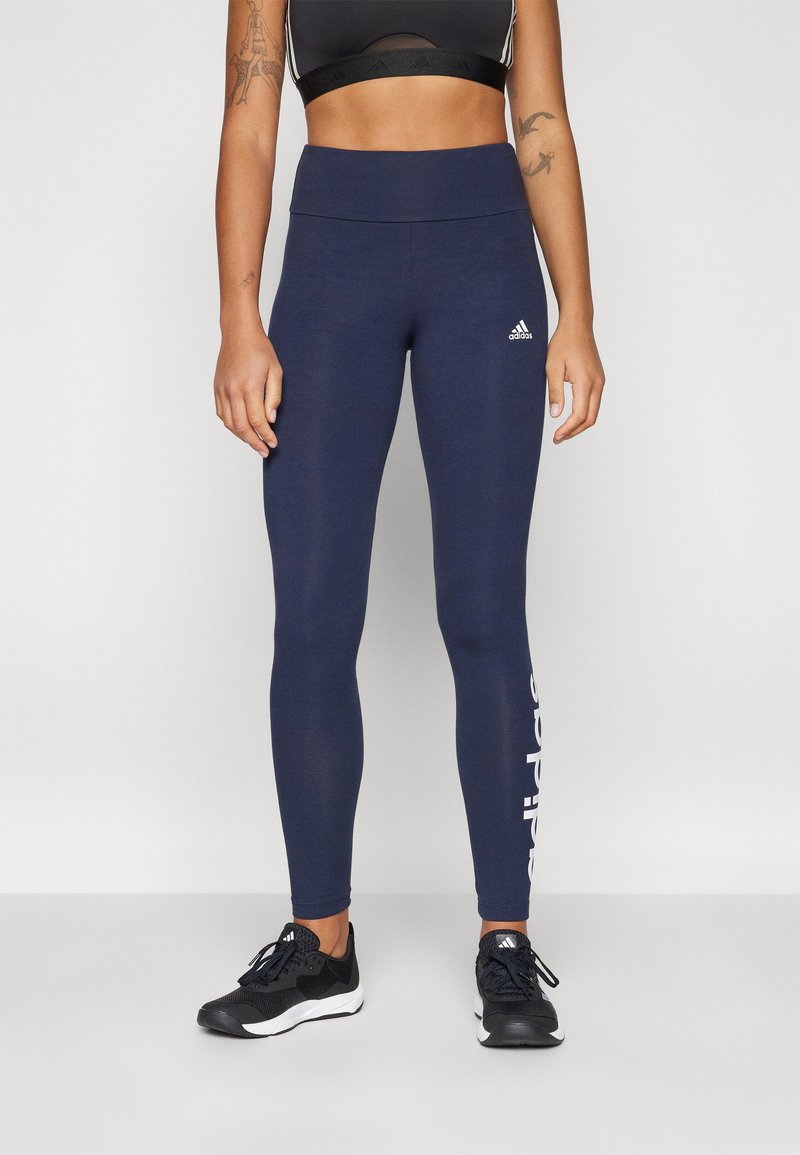 Jūriniai legginai, pagaminti iš elastingos medžiagos, su aukštu juosmeniu ir baltu „Adidas“ logotipu kairėje kojoje. Derinami su juodais sportiniais batais.