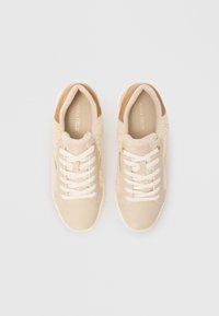 Baskets beige clair avec un côté en tissu texturé, des accents en cuir lisse, des lacets blancs et un design classique à bout rond.