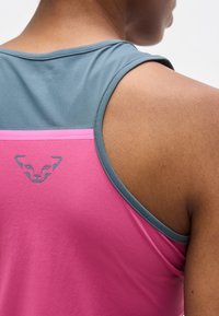 Κοντινό πλάνο στον ώμο και το πάνω μέρος της πλάτης ενός ατόμου που φορά αμάνικη ροζ και γκρι αθλητική μπλούζα με μικρό λογότυπο ζώου στην πλάτη.