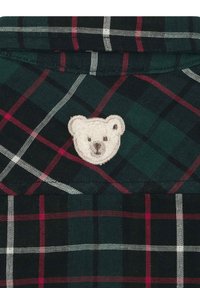 Camisa de cuadros verde y negra con líneas rojas y blancas, con un parche bordado de un oso de peluche texturizado en el cuello.