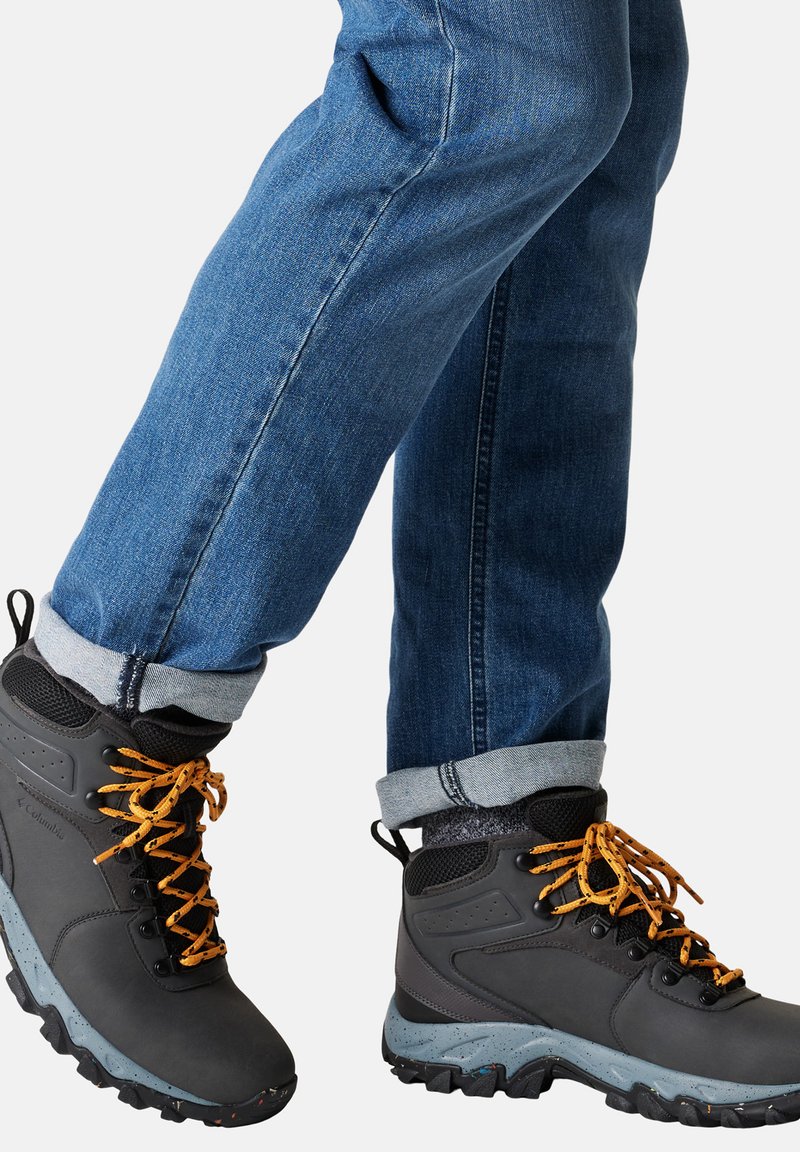 Le scarpe da trekking nere presentano lacci arancioni, una suola grigia maculata e una parte superiore testurizzata. Indossate con jeans in denim blu arrotolati.