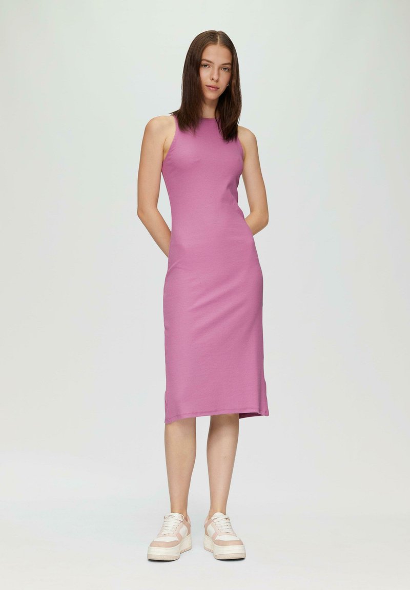 Rosa, ärmelloses Midikleid mit gerippter Textur und hohem Kragen, ausgestattet mit seitlichen Schlitzen und einer figurschmeichelnden Silhouette. Das Model trägt klobige Sneakers.