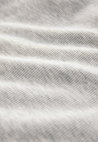 Gros plan d'un tissu gris clair doux avec de fines rayures diagonales foncées et des plis doux créant texture et profondeur.