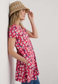 Kortebloemige roze tuniek met bloemdecoraties en bladerenpatronen, met een losse pasvorm en zijzakken, gecombineerd met een geweven strohoed.