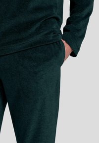 Sudadera de color verde oscuro, con textura, de corte relajado y mangas largas, combinada con pantalones jogger a juego que tienen bolsillos.
