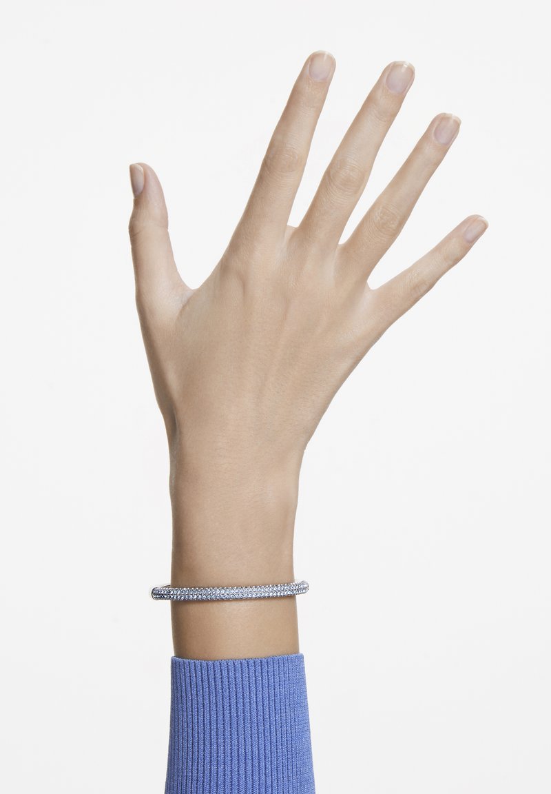 Bracelet en argent au design torsadé, ornée de petites pierres précieuses transparentes. Porté sur un poignet fin, associé à un pull bleu côtelé.