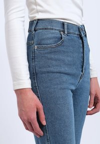 Hoch taillierte blaue Jeans aus Denim mit einer figurschmeichelnden Silhouette, die über ein klassisches Fünf-Taschen-Design und dezente Kontrastnähte verfügt.