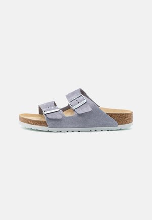 Grijze suède sandalen met twee verstelbare banden, zilverkleurige hardware, een kurken voetbed en een geribbelde rubberen zool. Zijaanzicht tegen een witte achtergrond.