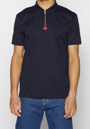 Marineblaues Polohemd mit Kragen und Halbreißverschluss, versehen mit einem roten Etikett am Hals. Hergestellt aus glattem Stoff, mit kurzen Ärmeln und klassischem Schnitt.