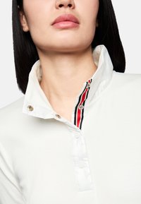 Weißes Poloshirt mit glänzendem Kragen, der rot und schwarz gestreift ist, mit Knopfverschluss und glatter Textur.