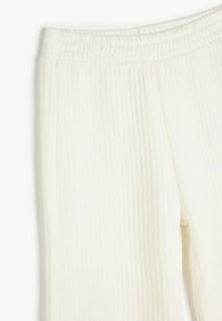 Pantalones de canalé crema con cintura elástica, que presentan una textura suave y un ajuste relajado, destacando líneas verticales y una apariencia ligera y aireada.