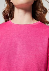 Fuchsia crew-neck sweatshirt made from soft fabric, featuring a smooth texture and a relaxed fit, visible near the neck area.