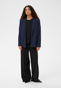 Jūras spēku zila žakete ar brīvu piegriezumu, ar iegrieztiem uzacīm un divām priekšējām kabatām, kombinēta ar melnu augšu un platām melnām biksēm, ar gludu tekstūru.