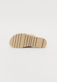 Beige-sandaalipohja vaakasuorilla urilla vetolujuuden parantamiseksi. Sisältää pyöristetyn varvasosan ja hienovaraisia teksturoituja yksityiskohtia. Tuotemerkki "Gabor" on painettuna.