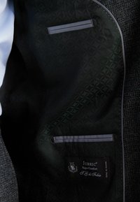 Interiorul jachetei negre cu un material texturat, având două buzunare și o etichetă cu inscripția "Jebric Super Comfort T.G. di Fabio."