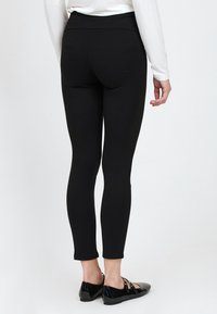 Zwarte leggings met een hoge tailleband, slim fit en rekbare stof. Gecombineerd met zwarte gepatineerde loafers met een decoratieve band.