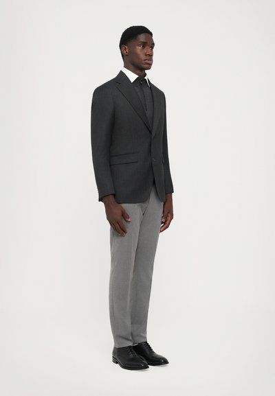 Costum elegant de culoare gri închis cu dungi, cămașă albă și pantaloni gri; completat cu pantofi negri, creând o apariție formală.