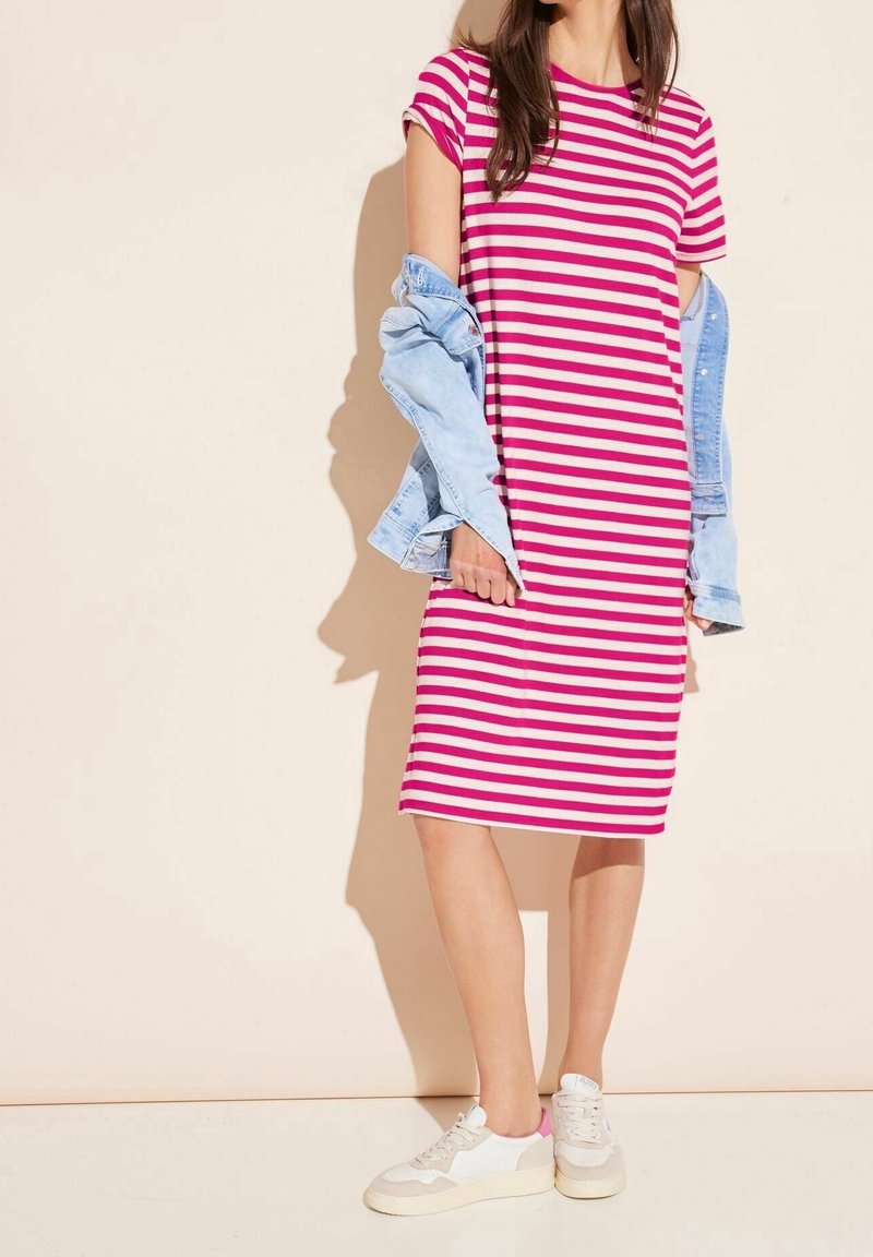 Sukienka w paski w kolorach różowym i białym, sięgająca do kolan, z krótkimi rękawami. Noszona z jasnoniebieską kurtką dżinsową i białymi trampkami. Gładka tkanina.