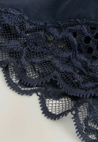 Dunkelblaues Spitzenborte mit komplexen Blumenmustern, gewellten Kanten und strukturiertem Mesh. Die Spitze zeigt feine Details und zarte Akzente.