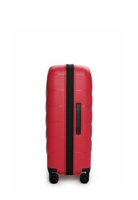 Červený kufr s tvrdou skořepinou, hladkým texturovaným povrchem, černým zipem, madlem na boku a čtyřmi otočnými koly pro snadnou manipulaci.