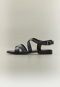 Czarne skórzane sandały z krzyżującymi się paskami, płaską podeszwą oraz regulowanym paskiem na kostce z klamrą zapewniającą pewne dopasowanie.