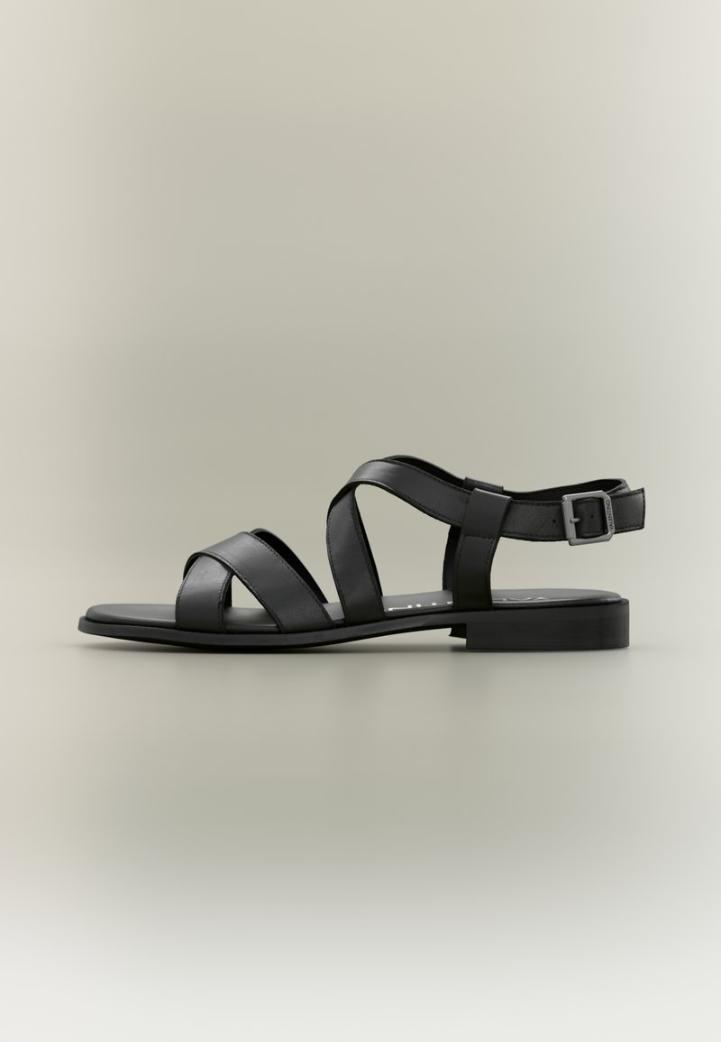 Czarne skórzane sandały z krzyżującymi się paskami, płaską podeszwą oraz regulowanym paskiem na kostce z klamrą zapewniającą pewne dopasowanie.