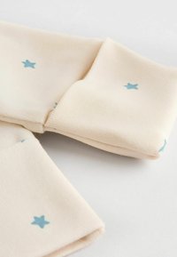 Beiger Stoff mit blauem Sternenmuster, mit umgeschlagenen Ärmeln. Das Material wirkt weich mit einer subtilen Textur.
