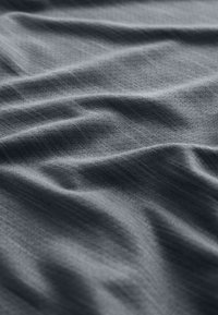 Gros plan sur un tissu texturé gris foncé avec des plis doux et un motif tissé subtil.