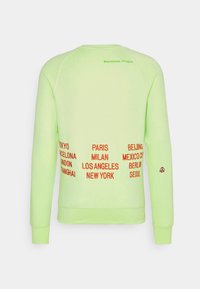 Světle zelený dlouhý svetr s dlouhým rukávem, na horní části zad nápis "Beaverton, Oregon" v zelené barvě a červené názvy měst vyšívané na dolní části zad a pravém rukávu.