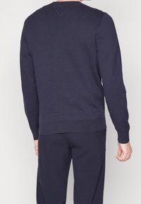 Granatowy sweter dzianinowy z długimi rękawami i okrągłym dekoltem. Posiada prążkowane mankiety i dół, bezszwowe plecy, delikatny detal w kształcie litery V przy dekolcie.