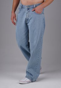 Helle blaue Jeans aus Denim mit lockerer Passform, sichtbarer Naht, Fünf-Taschen-Design und Kontrastnähten, kombiniert mit weißen Sneakers.