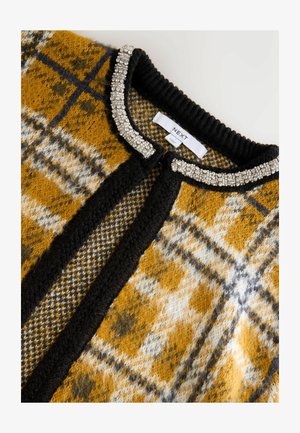 Kootud kardigan sinepi, musta ja halli ruudulisena tekstuuri viimistlusega; omab musta kraed, mis on kaunistatud hõbedaste pärlitega ja sildiga.