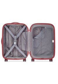 Interno di una valigia rossa con rivestimento a strisce grigie, cinghie incrociabili regolabili, una tasca con zip e un comparto in rete per una migliore organizzazione.