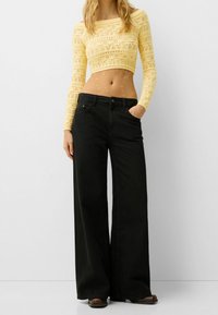 Czarne szerokie jeansy z talią o średnim stanie, zestawione z krótkim żółtym swetrem z dzianiny o fakturowanym wzorze i długich rękawach.