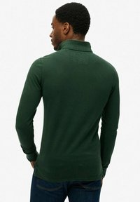 Groene long sleeve polo shirt met een geribbelde kraag, textured achterkant en een relaxed fit, gecombineerd met donkere jeans.