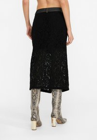 Jupe midi en dentelle noire avec un motif floral et une taille en denim, associée à des bottes métalliques en imprimé serpent jusqu'aux genoux et à des talons carrés.