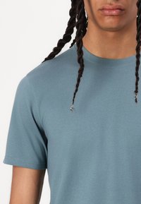 T-shirt azul claro com gola redonda em uma mistura suave de algodão. Mangas curtas com costuras planas. Close-up que mostra a textura do tecido e o detalhe da gola.