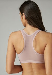 Lichtroze sportbeha met een racerback ontwerp, een gladde textuur en brede bandjes, met minimale naden en een elastische band aan de onderkant.