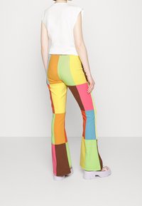 Pantalons évasés colorés avec un motif en patchwork comportant des teintes vives de jaune, vert, rose, marron et bleu. Fabriqués à partir d'un matériau doux et extensible.