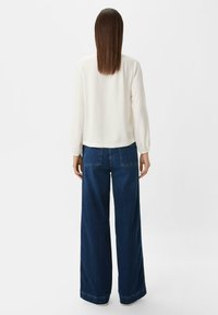 White long-sleeve blouse with gathered cuffs, paired with wide-leg dark blue denim jeans featuring rear pockets and a relaxed fit.