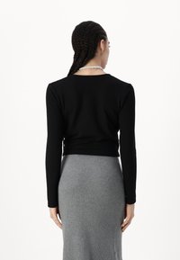 Svart långärmad topp med figurnära design, kombinerad med en grå ribbad kjol. Toppen har rund halsringning och figurnära ärmar.