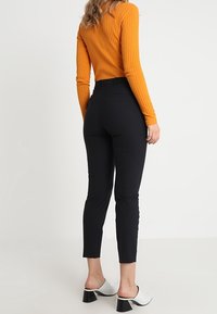 Musta istuva housut yhdistettynä ribbed-tekstiilistä valmistettuun, palavasta oranssista pitkähiharaiseen puseroon. Puseron kankaassa on tekstuuria ja se on tiukka yltäkylläinen.