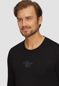 Zwarte lange mouwen T-shirt met een ronde hals, voorzien van geborduurde tekst in een contrasterende kleur op de borst. Glad stofstructuur.