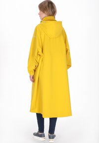 Sárga vízálló esőkabát kapucnival, hosszú ujjakkal és laza szabással. Rugalmas mandzsettákat és szabályozható, húzott derekat tartalmaz.